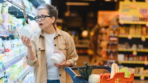 Woman standing in a grocery store aisle, comparing product labels and making informed decisions about healthy food items for her family