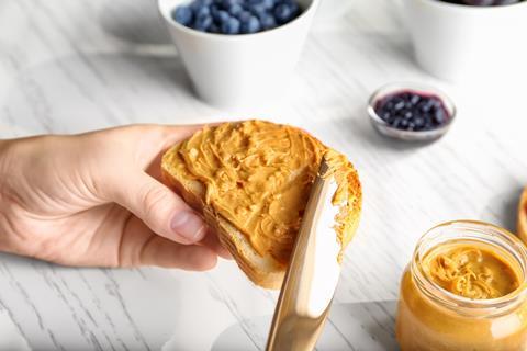 Woman,Spreading,Peanut,Butter,On,Slice,Of,Bread,Near,Kitchen