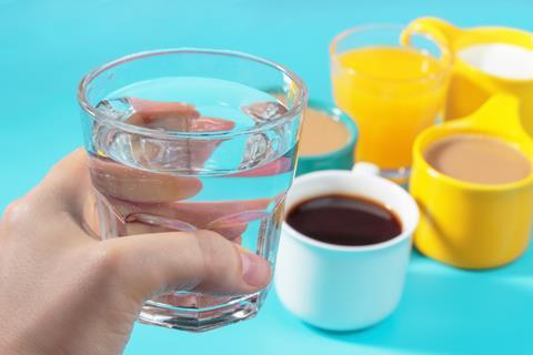 Female,Hand,Holds,A,Glass,Of,Water,On,The,Background