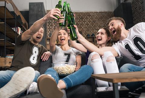 Happy,Young,Friends,Clinking,Beer,Bottles,While,Sitting,On,Sofa
